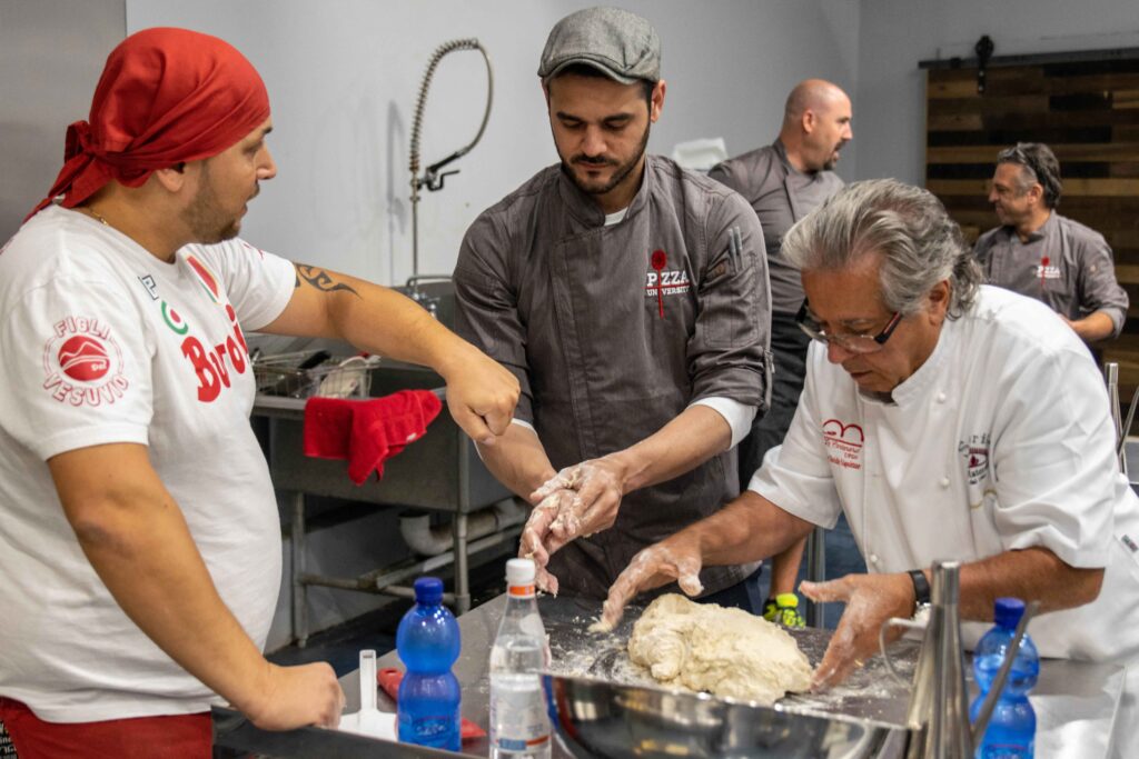 two italian chefs teach Pizza University student how to stretch neapolitan dough