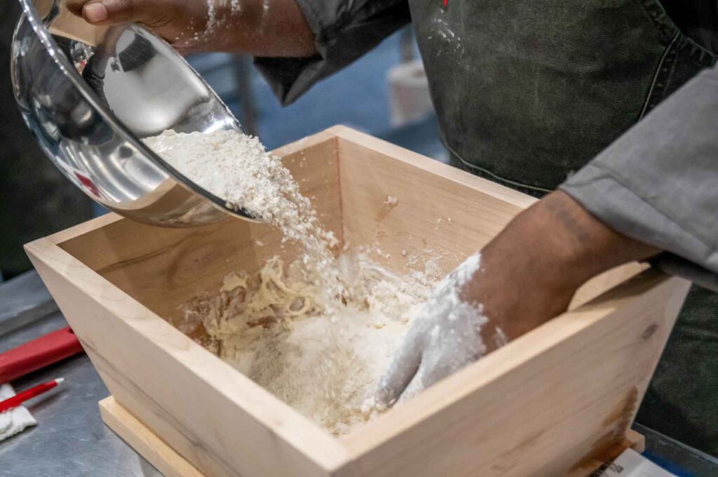 African American man mixes water and flour in a wooden basin