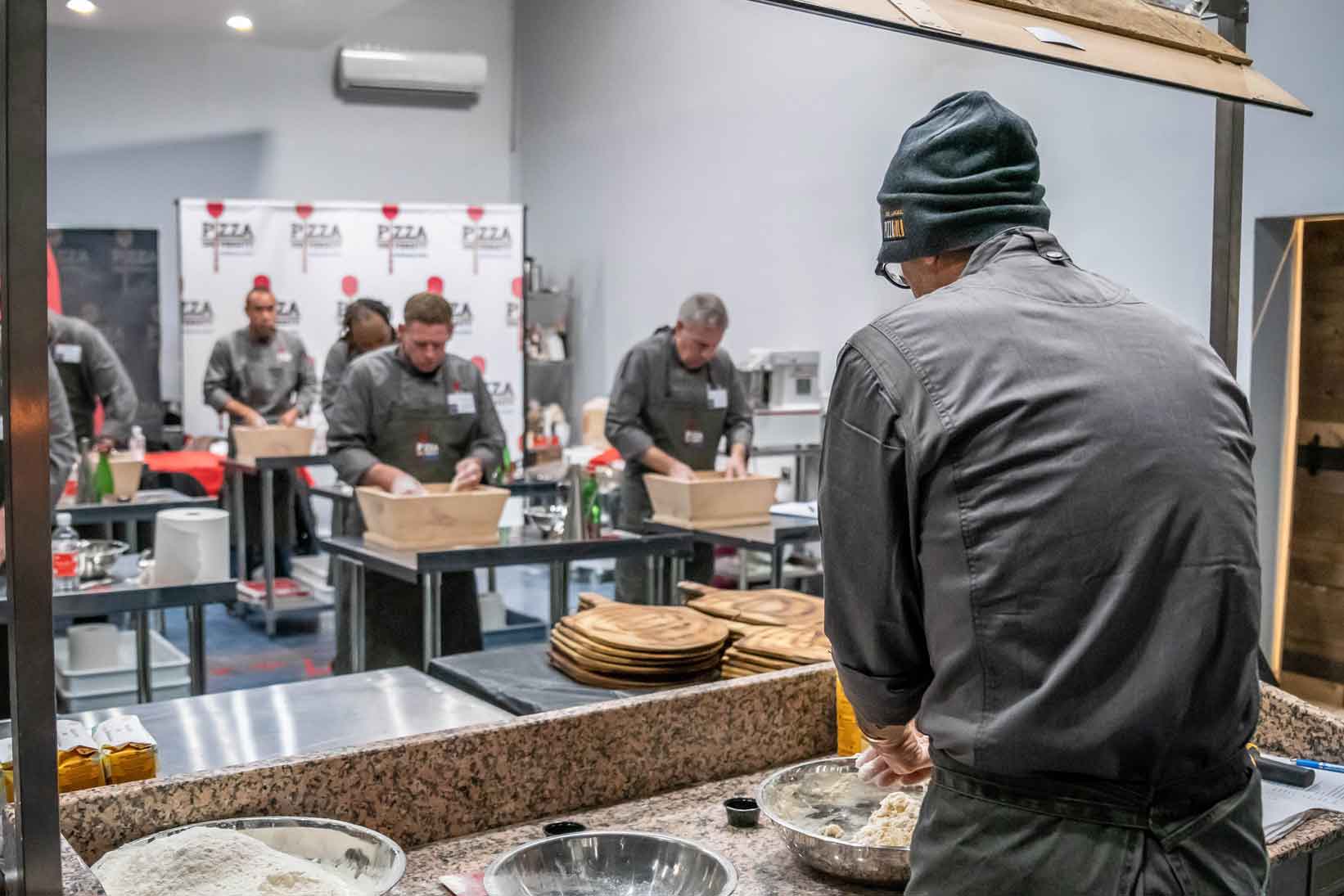 Chef instructor stands under mirror to teach students how to properly mix dough