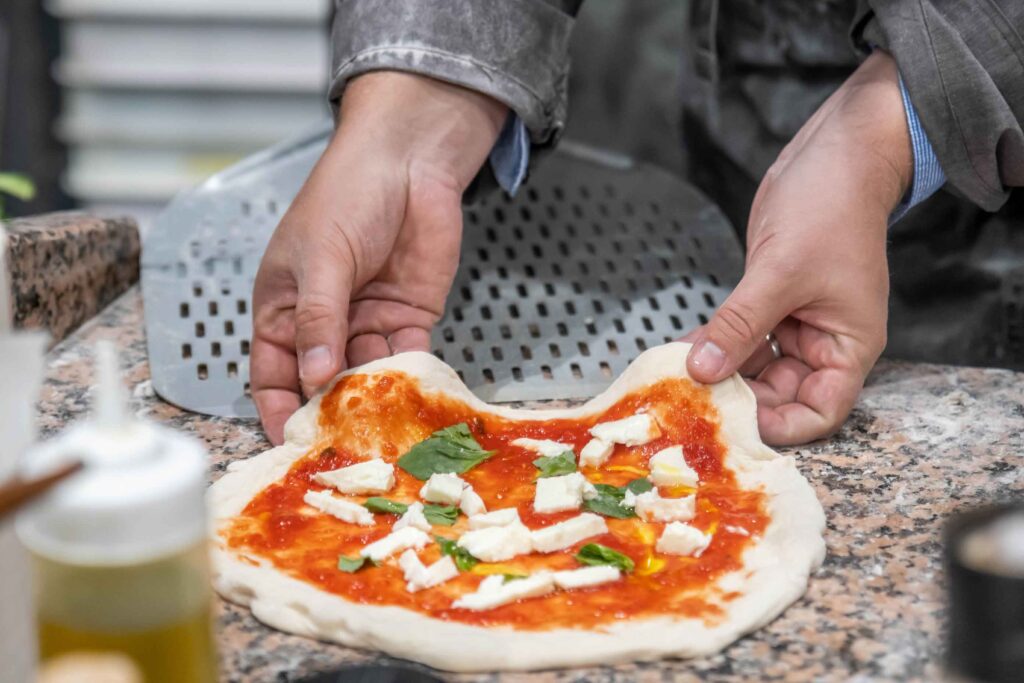 Female hands pull uncooked margherita pizza on a peel